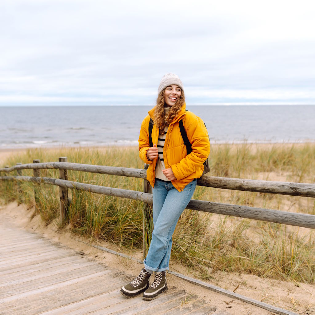 Frau lehnt an Holzzaun in Dünenlandschaft am Meer