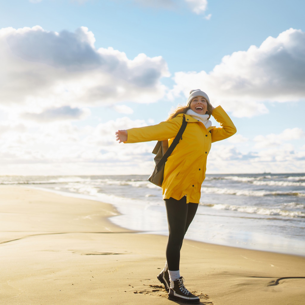 Frau in gelber Jacke mit Rucksack am Strand