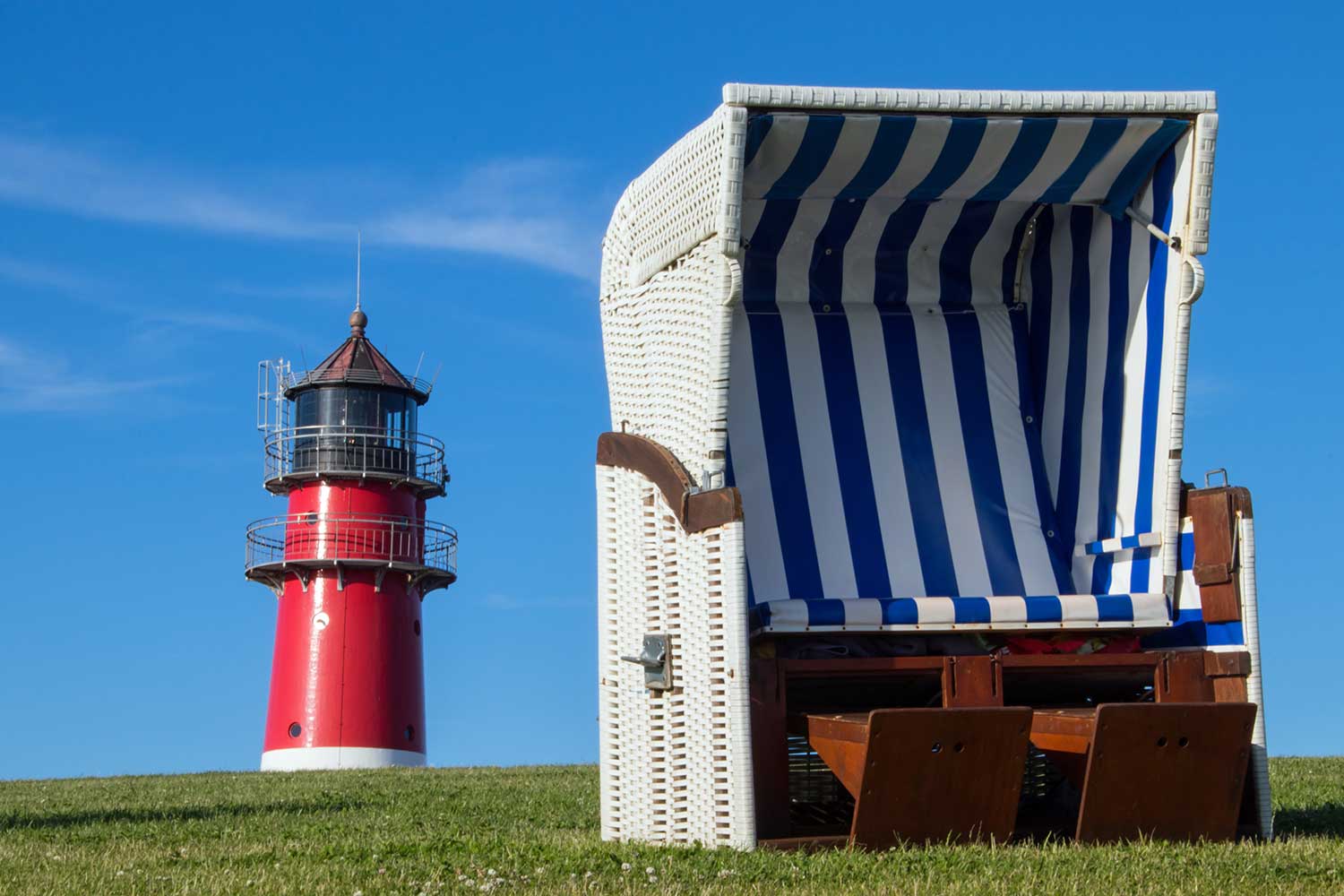 Die Spitze des Leuchturms ragt über den Deich auf dem ein-Strandkorb steht.