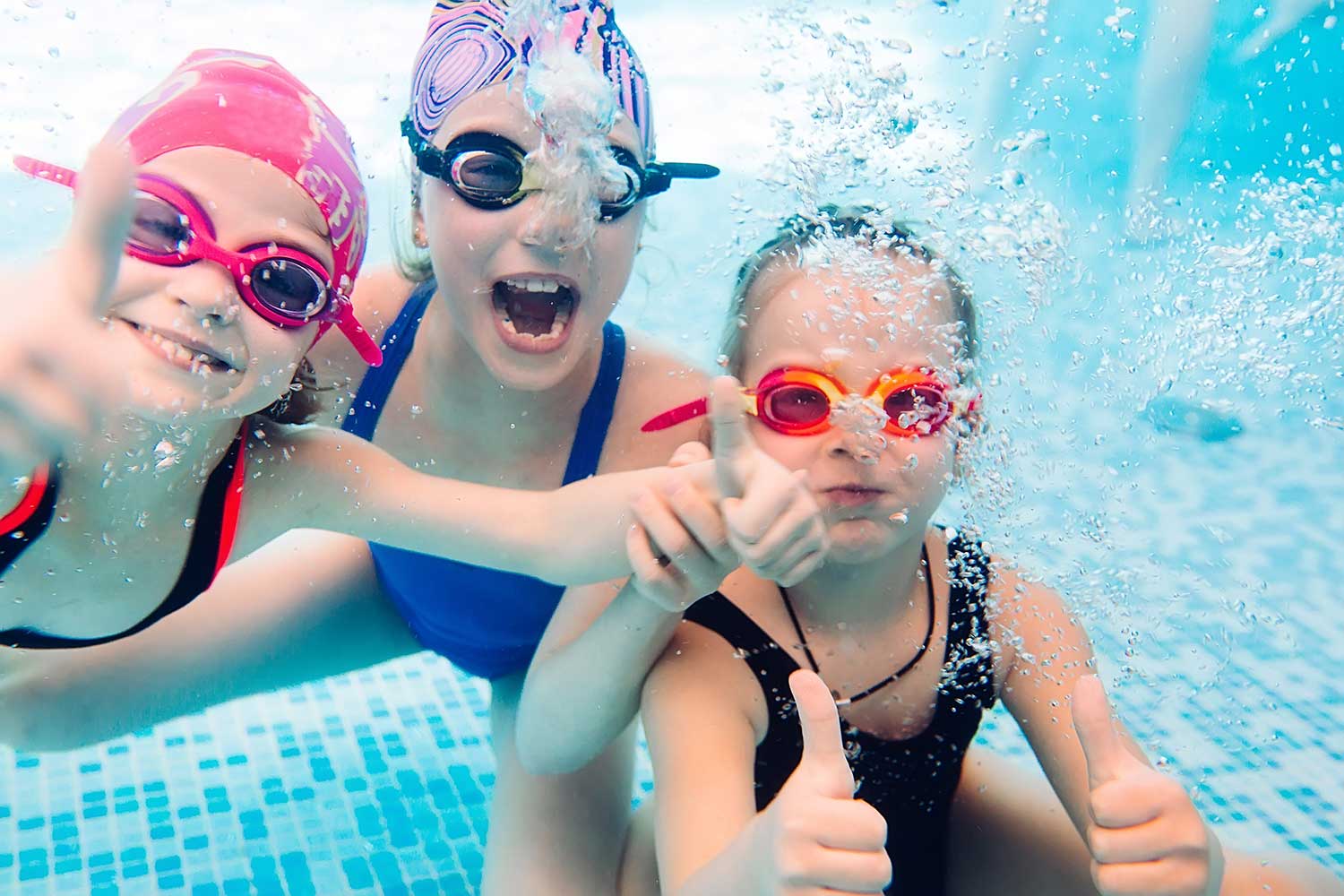 Drei fröhliche Mädchen beim Tauchen im Schwimmbecken.