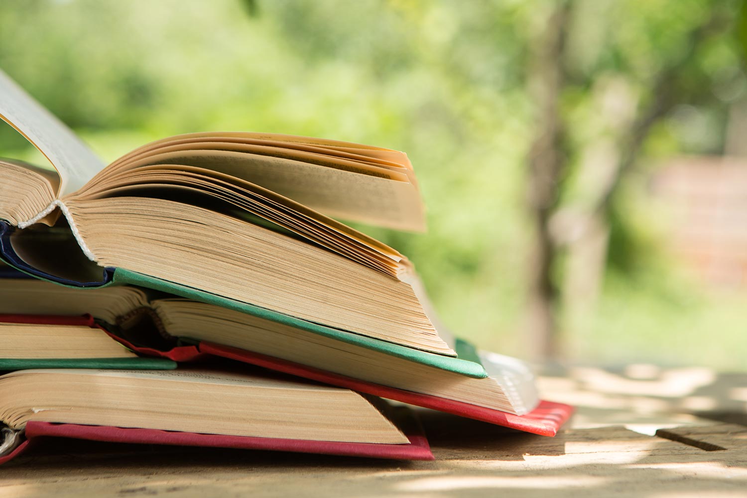 Ein Stapel geöffneter Bücher auf einem Tisch im Garten.