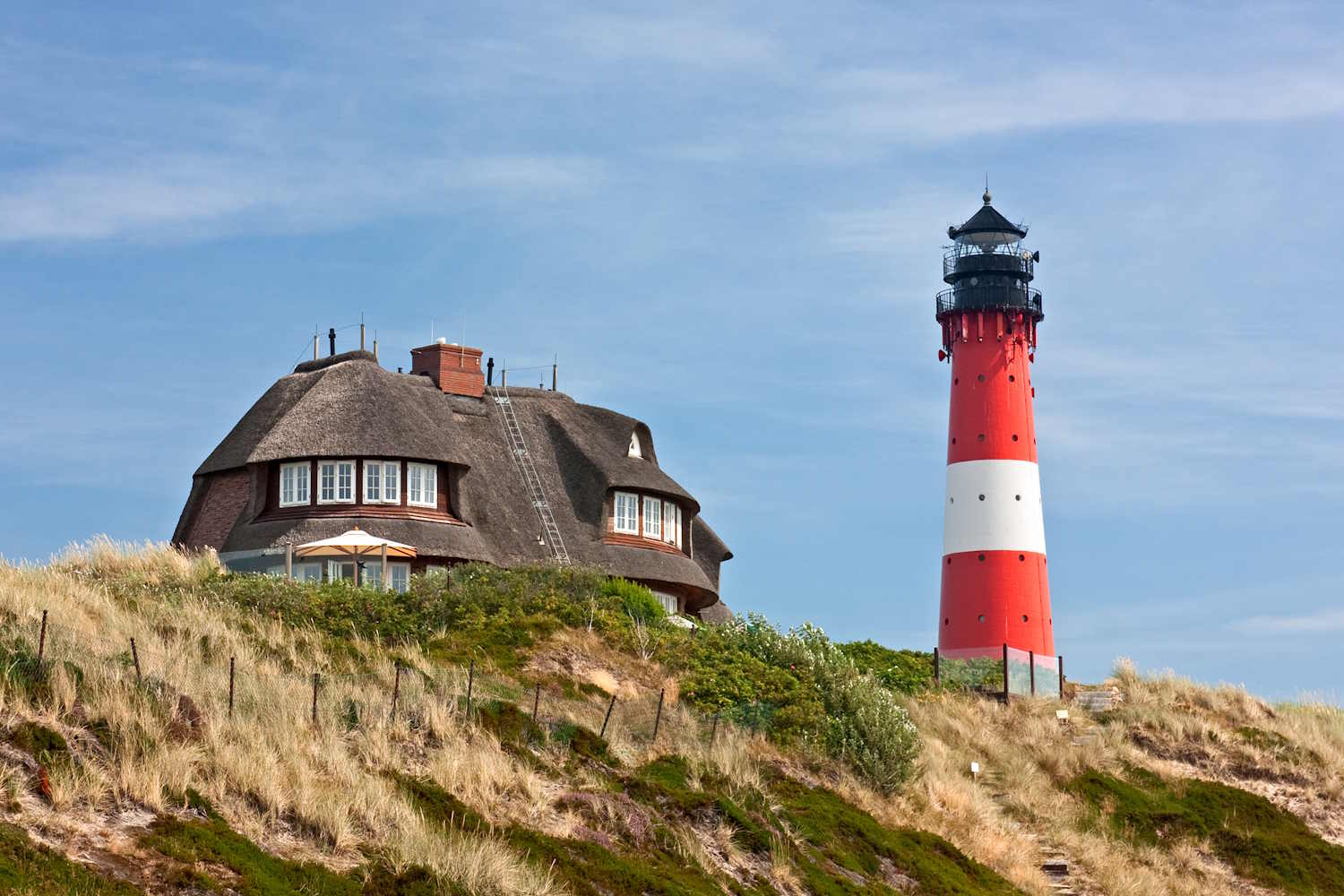 Leuchtturm in Hörnum mit Reetdachhaus im Hintergrund