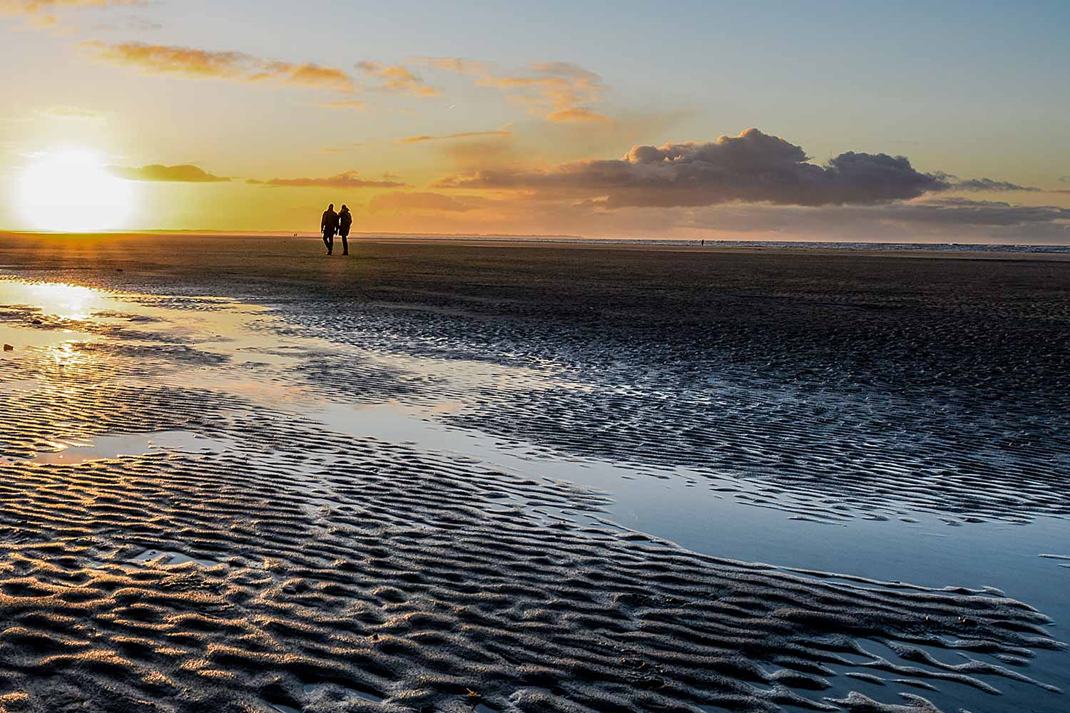 Sonnenuntergangsstimmung am Wattenmeer, zwei Wattwanderer sind am Horizont zu sehen.